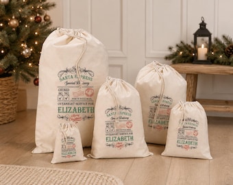May include: A set of five off-white drawstring gift bags in varying sizes, each printed with Santa Express Special Delivery graphics, North Pole mail stamps, and the name Elizabeth in green text, featuring a checked once twice checkbox design.
