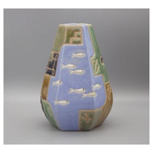 May include: A ceramic vase with a distinctive geometric design. The vase has a light blue central panel with white fish, framed by green, brown, and blue sections. The vase has a textured surface and a wide base.