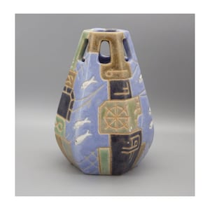 May include: A ceramic vase with a unique, geometric design. The vase features a light blue background with dark blue, green, and brown accents. White fish and a ship's wheel are depicted on the surface. The top has cut-out sections.
