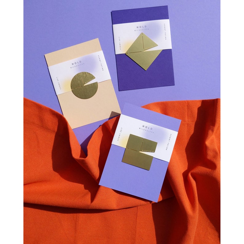 May include: Three purple cards with the word "MOLD" and a gold geometric shape on each. The cards are on a bright orange fabric surface.