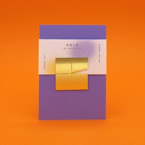 May include: A gold metal picture holder with the text "HOLD BILDHALTER" and "NIUSTUDIO" on a purple background.