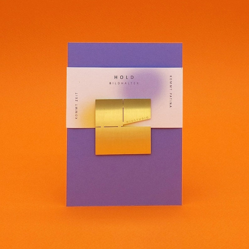 May include: A gold metal picture holder with the text "HOLD BILDHALTER" and "NIUSTUDIO" on a purple background.