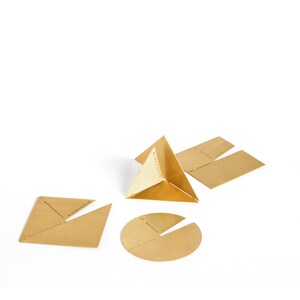 May include: A set of four brass geometric shapes, including a pyramid, a square, a circle, and a rectangle. Each shape has a unique design and is marked with the text "OBJECTSETH".