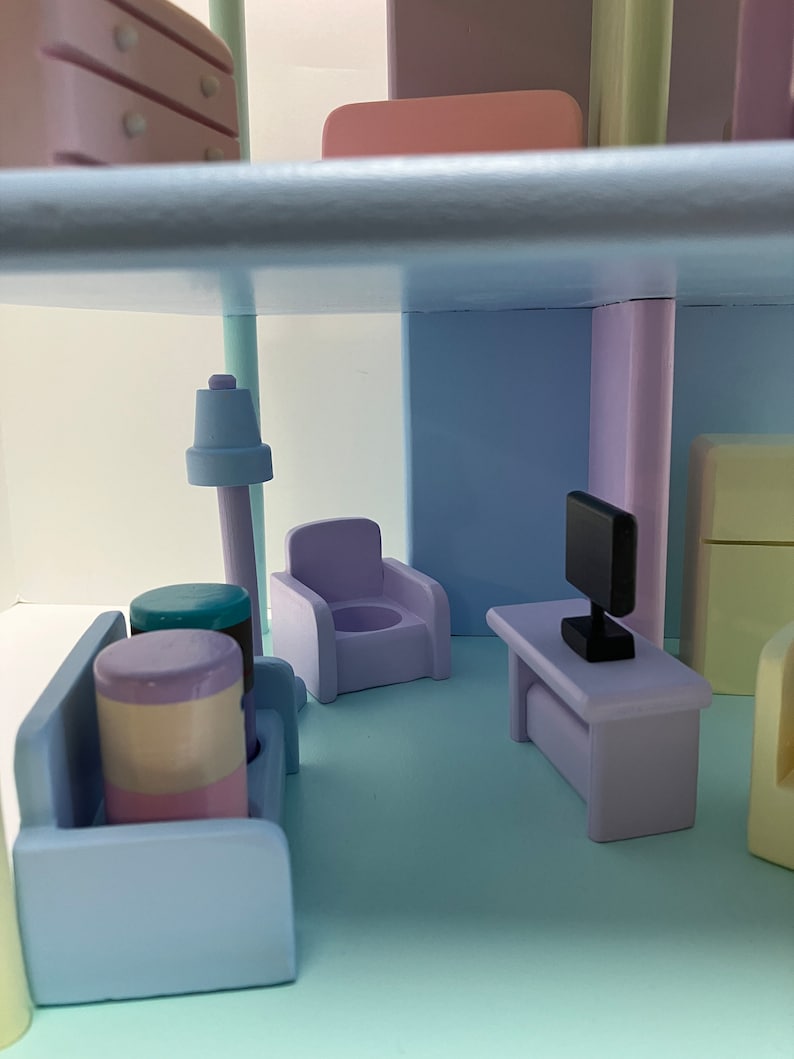 May include: A miniature dollhouse interior with pastel-colored furniture. The scene includes a sofa, armchair, table with a TV, and a lamp. The color palette features shades of blue, purple, and pink, creating a soft and inviting atmosphere.