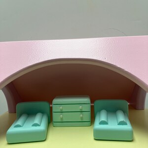 May include: A miniature dollhouse bedroom set with a light pink arched roof. The set includes two mint green beds with pillows and a matching dresser with two drawers. The furniture sits on a yellow surface.