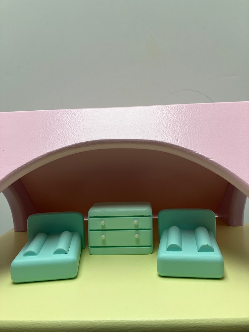 May include: A miniature dollhouse bedroom set with a light pink arched roof. The set includes two mint green beds with pillows and a matching dresser with two drawers. The furniture sits on a yellow surface.