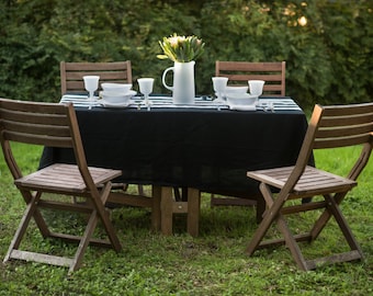 May include: A black and white striped tablecloth covers a wooden table with four chairs. The table is set with white plates, glasses, and silverware. A vase with white flowers sits in the center of the table.