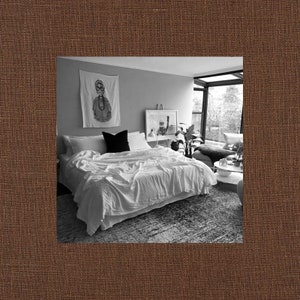 May include: A white bed with white bedding and a black throw pillow in a bedroom with a large window, a white rug, and a framed print on the wall.