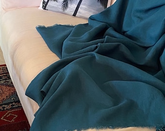 May include: A teal blue throw blanket with a fringed edge is draped over a white couch. A white pillow with a black and white palm tree print is on the couch.