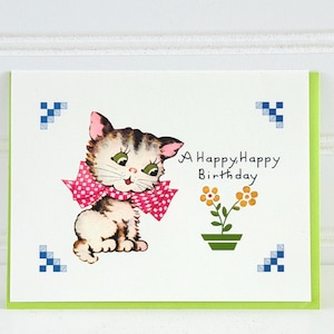 May include: A Happy Birthday greeting card featuring a vintage illustration of a kitten wearing a pink bow. The card has a green border and includes a small flower pot with orange flowers.