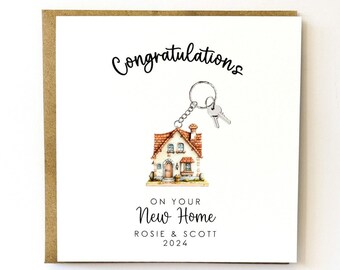 May include: A white card with a brown border. The card has a drawing of a small house with a key attached to it. The text on the card reads "Congratulations on your New Home Rosie & Scott 2024".