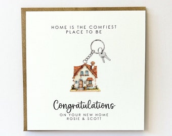 May include: A white card with brown trim features a house-shaped keychain with two silver keys. The card reads "Home is the comfiest place to be" and "Congratulations on your new home Rosie & Scott".