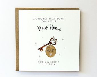 May include: A white card with a gold key and tag that says "No. 27" with a heart. The card says "Congratulations on your New Home" and "Rosie & Scott July 2024".