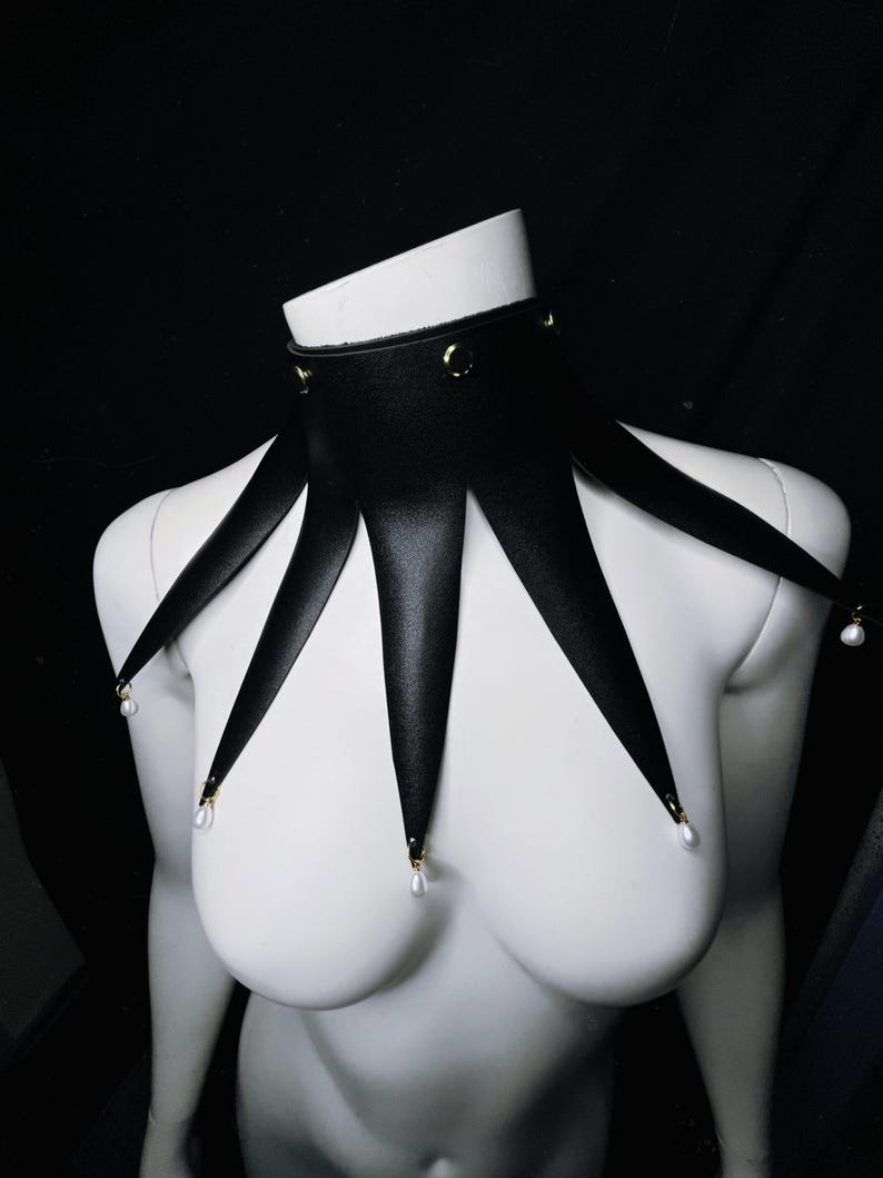 May include: A black leather choker with five points extending down, each ending with a pearl. The choker has gold accents.