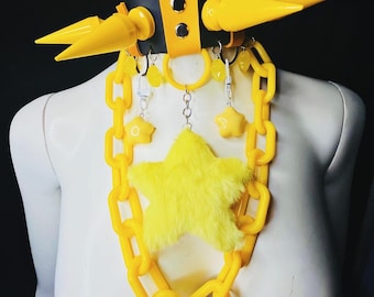 May include: A yellow and black choker necklace with a chain and star pendant. The choker features yellow spikes and a yellow chain with a fluffy star pendant. The necklace is displayed on a white mannequin.