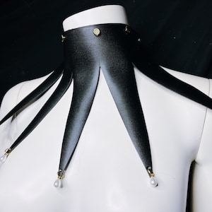 May include: A black satin choker with five points, each ending in a small white pearl. The choker has gold accents.