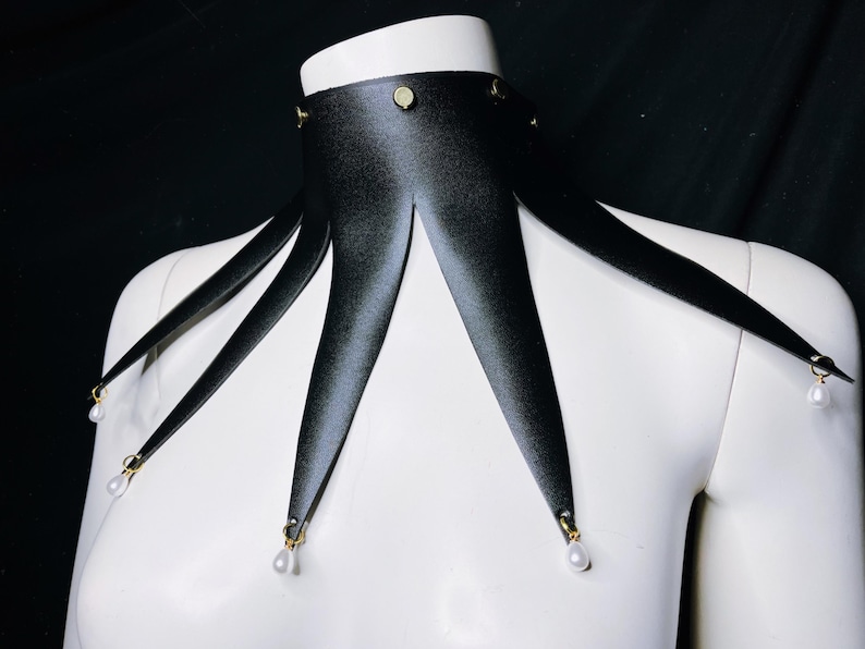 May include: A black satin choker with five points, each ending in a small white pearl. The choker has gold accents.