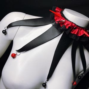 May include: A black choker necklace with red ribbon and spikes, with black ribbon straps that have red and black beads hanging from them.