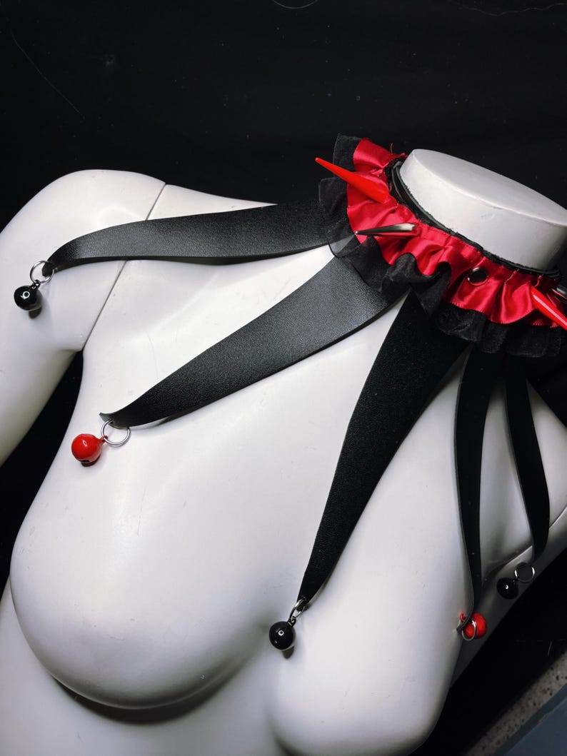 May include: A black choker necklace with red ribbon and spikes, with black ribbon straps that have red and black beads hanging from them.