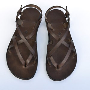 Op de afbeelding: Een paar bruine leren sandalen met gekruiste banden. De sandalen hebben een eenvoudig ontwerp en zijn gemaakt van hoogwaardig leer.