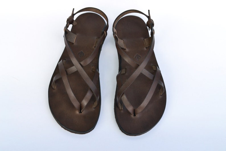 Op de afbeelding: Een paar bruine leren sandalen met gekruiste banden. De sandalen hebben een eenvoudig ontwerp en zijn gemaakt van hoogwaardig leer.