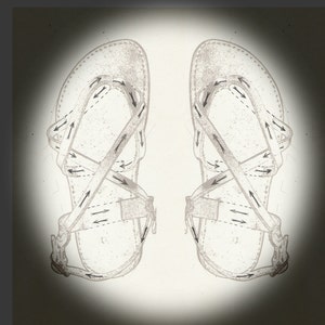 Op de afbeelding: Een paar zwarte leren sandalen met gekruiste banden en een gespsluiting. De banden zijn versierd met pijlen die de richting aangeven om de banden door te halen.