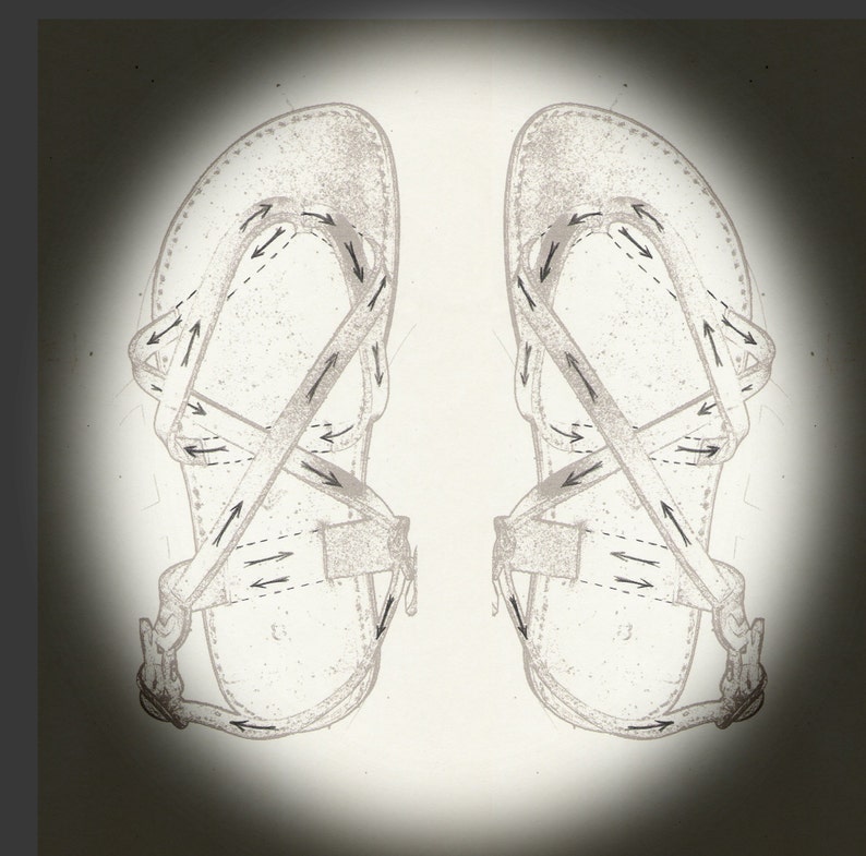 Op de afbeelding: Een paar zwarte leren sandalen met gekruiste banden en een gespsluiting. De banden zijn versierd met pijlen die de richting aangeven om de banden door te halen.