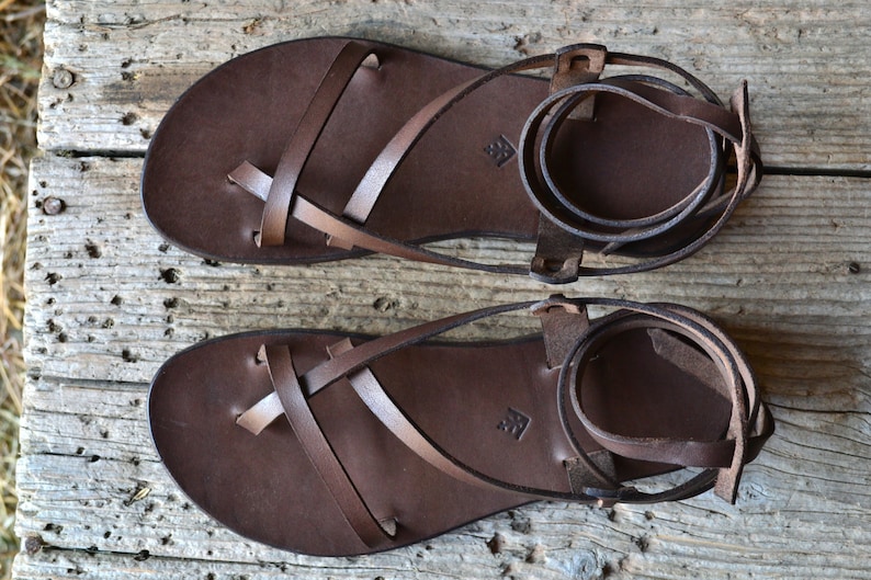 May include: A pair of brown leather sandals with criss-cross straps and ankle ties.