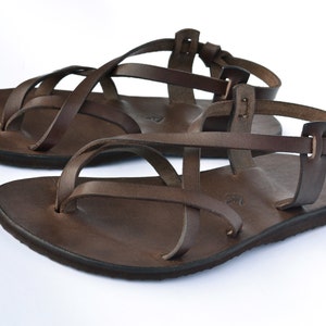Op de afbeelding: Bruine leren sandalen met meerdere banden die over de voet en enkel kruisen. De sandalen hebben een eenvoudig ontwerp en een platte zool.