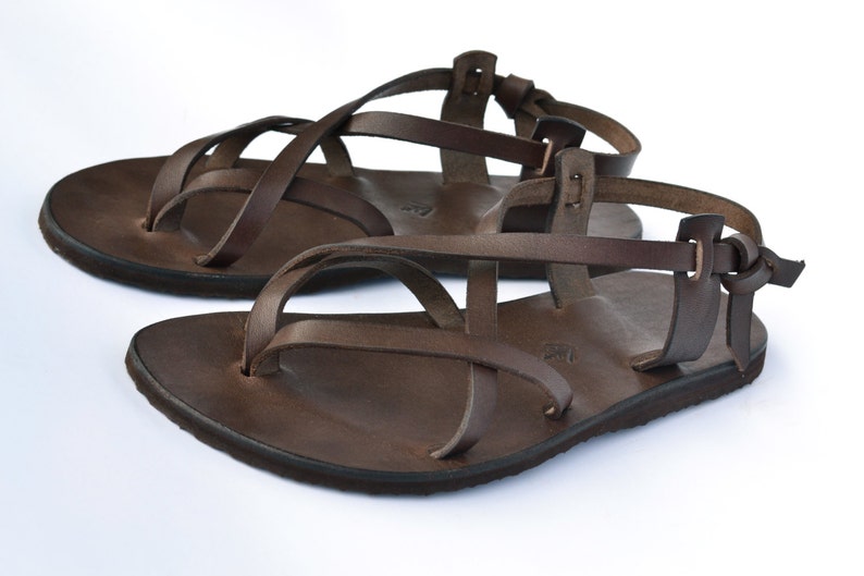 Op de afbeelding: Bruine leren sandalen met meerdere banden die over de voet en enkel kruisen. De sandalen hebben een eenvoudig ontwerp en een platte zool.