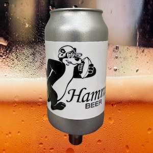 May include: A silver can with a black and white cartoon bear wearing a hat and holding a football. The can has a white label with the text "Hamm's Beer".