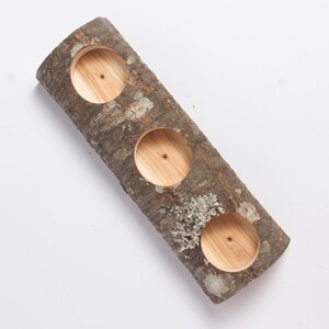 Puede incluir: Un portavelas de tronco de madera con tres recortes circulares para velas. El tronco es marr&oacute;n y tiene una textura de corteza natural.