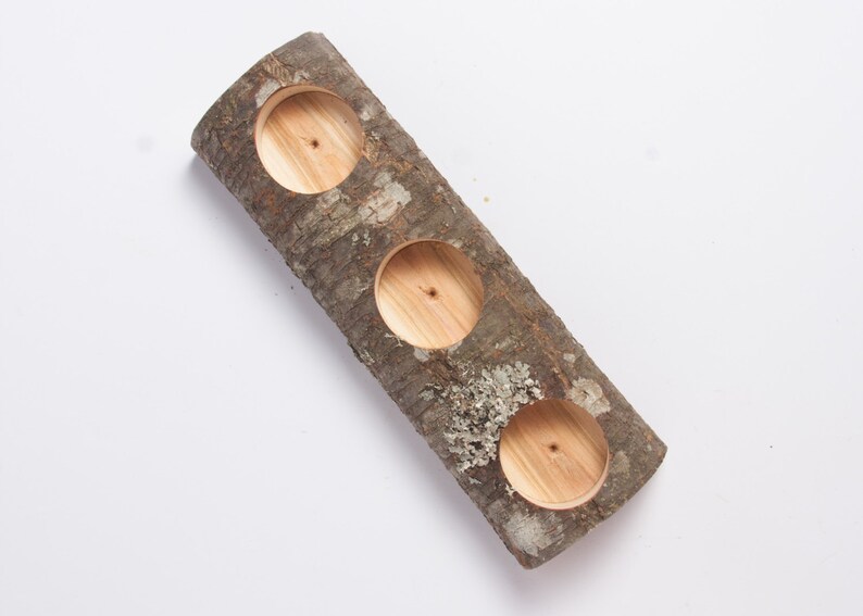 Puede incluir: Un portavelas de tronco de madera con tres recortes circulares para velas. El tronco es marr&oacute;n y tiene una textura de corteza natural.