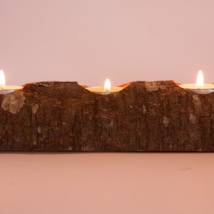 Puede incluir: Un portavelas de madera con tres velas de t&eacute; encendidas. El portavelas est&aacute; hecho de un tronco natural con una textura de corteza rugosa.