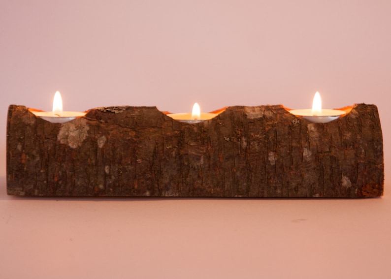 Puede incluir: Un portavelas de madera con tres velas de t&eacute; encendidas. El portavelas est&aacute; hecho de un tronco natural con una textura de corteza rugosa.