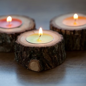 Könnte beinhalten: Drei Kerzenhalter aus Holz mit Teelichtern. Die Kerzenhalter sind aus Baumrinde gefertigt und haben eine natürliche Holzoptik. Die Kerzen sind angezündet und die Flammen sind sichtbar.
