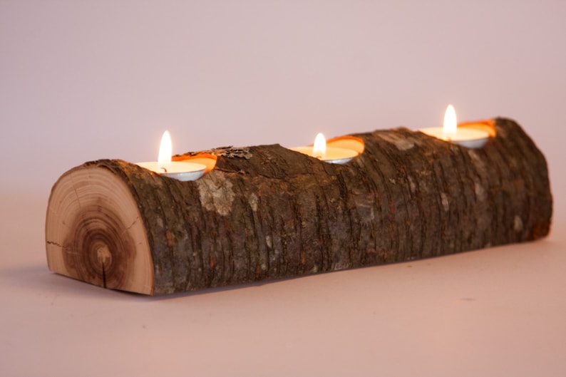Puede incluir: Un portavelas de madera r&uacute;stico con tres portavelas para velas de t&eacute; tallados en la madera. El portavelas est&aacute; hecho de un tronco natural con la corteza todav&iacute;a en &eacute;l. Las velas est&aacute;n encendidas y brillan.