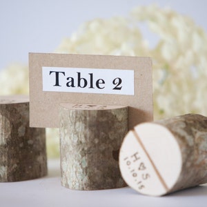 Puede incluir: Porta número de mesa de madera rústica con una tarjeta marrón que dice "Mesa 2".