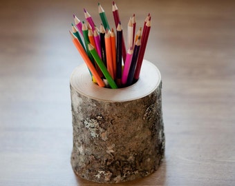May include: A wooden pencil holder made from a tree trunk with a natural bark finish. The holder is filled with a variety of colored pencils.
