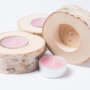 Könnte beinhalten: Drei Kerzenhalter aus Holz, hergestellt aus Birkenrinde, mit rosa Teelichtern darin.