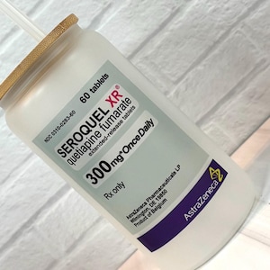 May include: A white prescription bottle with a bamboo lid and a straw. The label reads "SEROQUEL XR" and "300mg*Once Daily". The bottle contains 60 tablets of quetiapine fumarate, an extended-release medication.