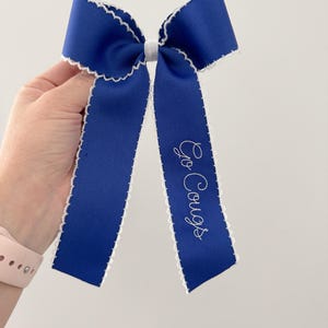 Può includere: Un fiocco di nastro blu reale con bordi smerlati bianchi e la scritta ricamata "Go Cougs". Il fiocco è legato con un nodo centrale bianco. Questo accessorio per capelli è perfetto per il giorno della partita o per l'uso quotidiano.