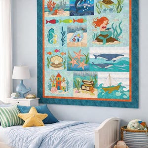 Puede incluir: Un edredón cuadrado y colorido con un tema de vida marina, con imágenes de delfines, sirenas y varias criaturas marinas. El edredón está bordeado con una tela verde azulado y un ribete naranja, y cuelga sobre la cama de un niño. Es un artículo decorativo.