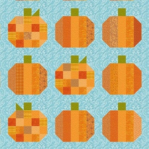 May include: A quilt pattern featuring 25 orange and brown patchwork pumpkins on a light blue background. The quilt is signed "Angie Padilla" in the bottom centre.