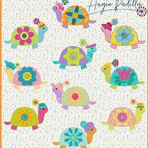 Może przedstawiać: Kolorowy kocyk z białym tłem i powtarzającym się wzorem małych białych kropek. Kocyk przedstawia dziewięć naszytych żółwi z różnymi wzorami kwiatowymi i geometrycznymi. Żółwie noszą kapelusze i mają kwiaty na swoich pancerzach. Kocyk jest otoczony turkusową ramką z powtarzającym się wzorem białych trójkątów. Kocyk jest podpisany "Angie Padilla" w prawym górnym rogu.