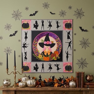 May include: A square fabric wall hanging featuring a central circular illustration of a witch with pink hair wearing a floral hat, surrounded by pumpkins and leaves. The border displays black witch silhouettes and pumpkins on a grey patterned background.
