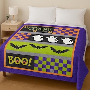 Può includere: Una coperta a tema Halloween con bordo viola. Il design presenta le parole "creepy" e "BOO!" in giallo e arancione, insieme a fantasmi bianchi e pipistrelli neri su sfondo verde e grigio. Quadri arancioni e viola a scacchi completano il design.