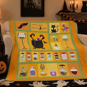 May include: A rectangular quilt featuring a yellow and orange background with various Halloween-themed appliqués including a black cauldron, a cat, a crystal ball, potion bottles, jars with specimens, and the text Come and sit for a spell.
