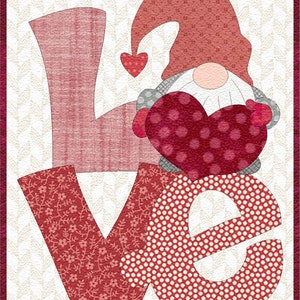 Könnte beinhalten: Ein roter, weißer und rosafarbener Patchwork-Quiltblock mit dem Wort "LOVE" in großen Buchstaben. Ein roter Zwerg mit weißem Bart hält ein rotes Herz mit weißen Punkten vor dem "O". Der Hintergrund ist ein weiß-graues Muster.