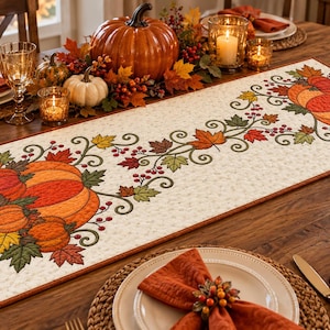 May include: A rectangular fabric table runner featuring a cream-colored background with a repeating pattern of orange pumpkins, green and yellow autumn leaves, and red berries. The runner has a thin brown border and a quilted texture.